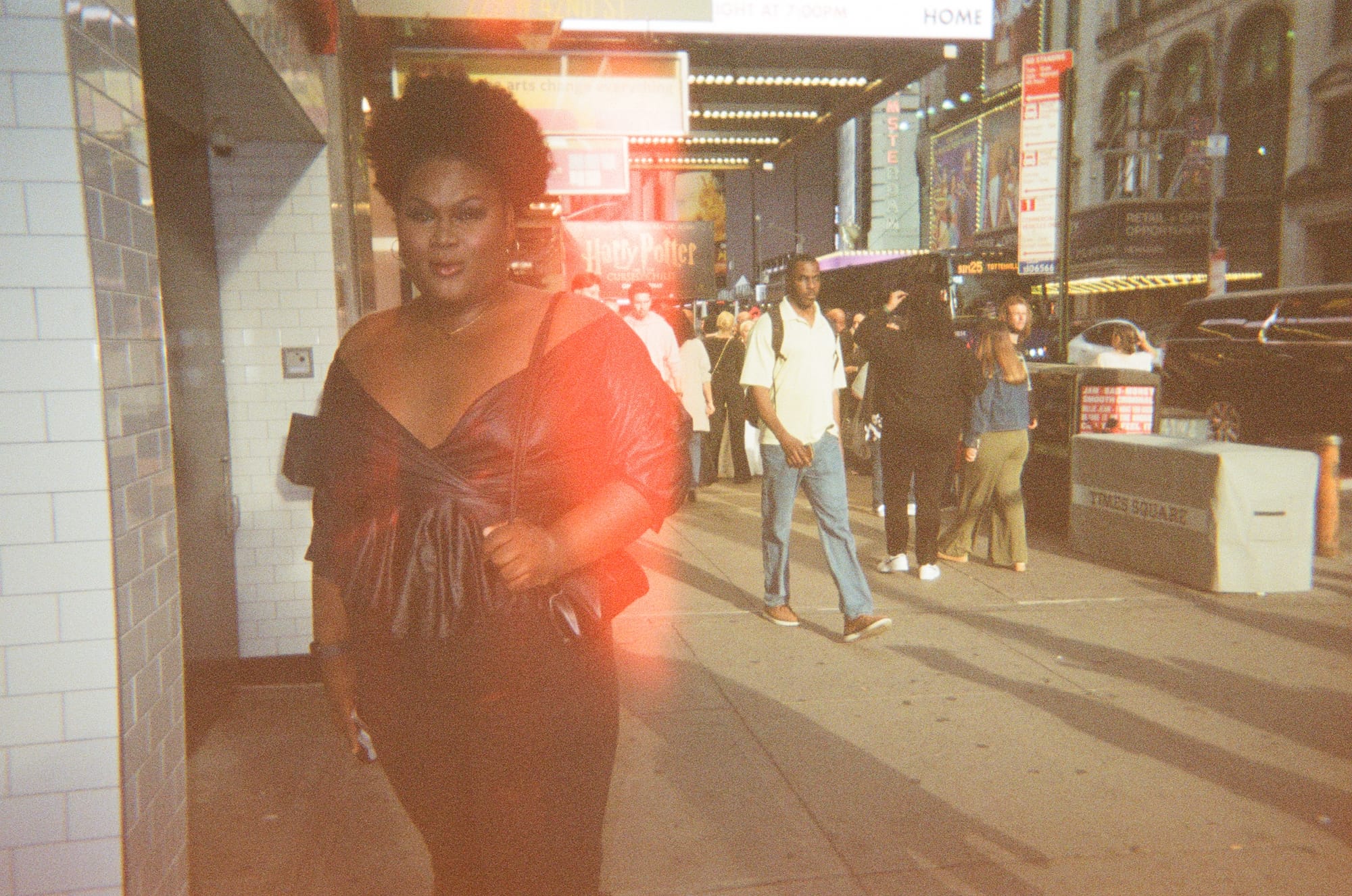 A Black Trans Woman wearing a off the shoulder brown leather top with her hair natural, posing on the street in New York Cityin New York City