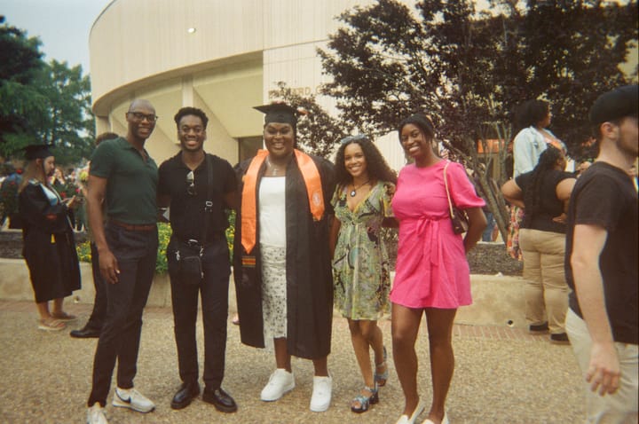 Sis the doll in her cap and gown smiling for the camera, surrounded by her best friends